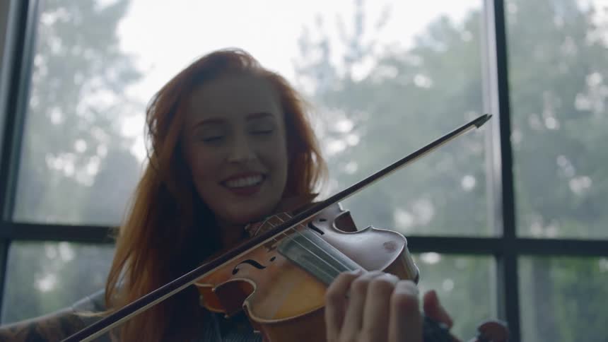 A red haired woman smiles as she plays a violin