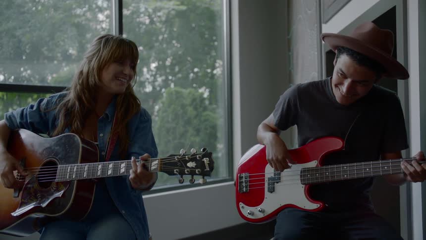A woman plays guitar while a man in a hat plays bass