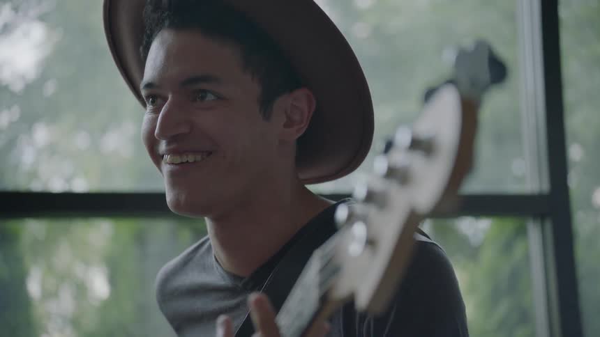 A man plays a bass guitar in front of a window