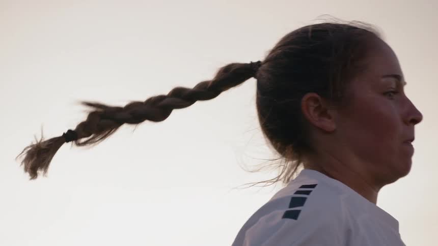 Woman football player with white football uniform plays football in the football field at dusk