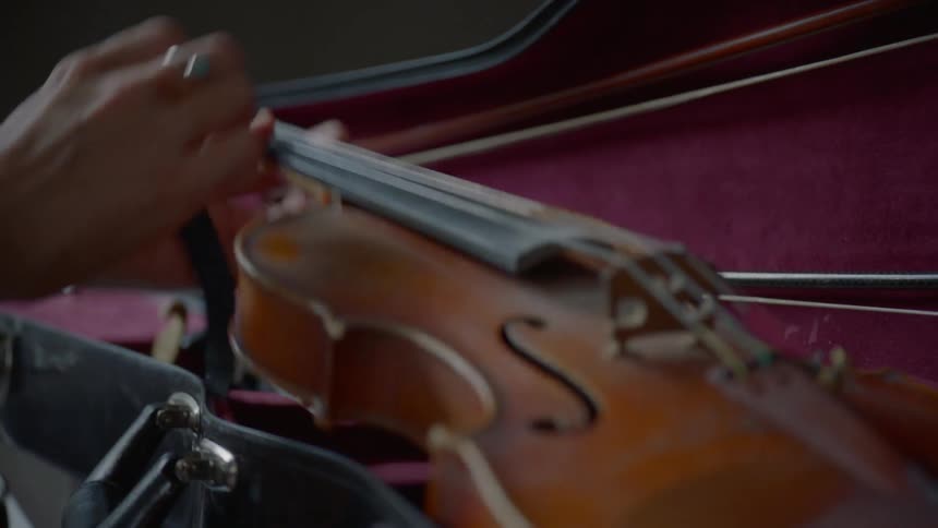 A person takes the strap off of a violin and takes it out of the case