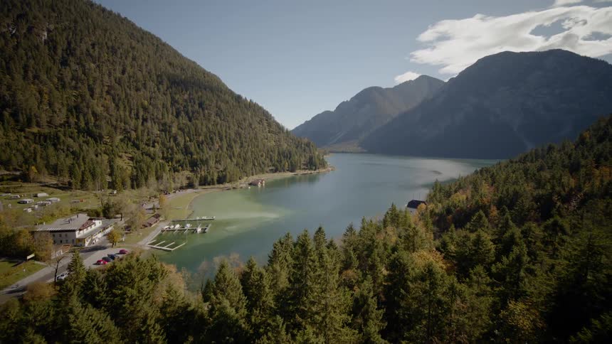 The camera flies over trees next to a mountain lake and dock
