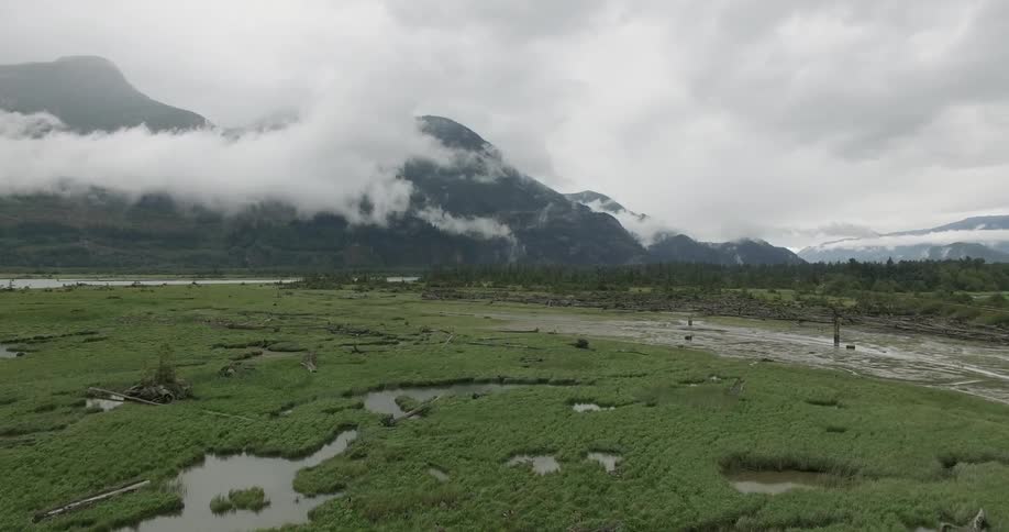 Aerial footage of a boggy area and low-lying clouds that are hugging mountain peaks
