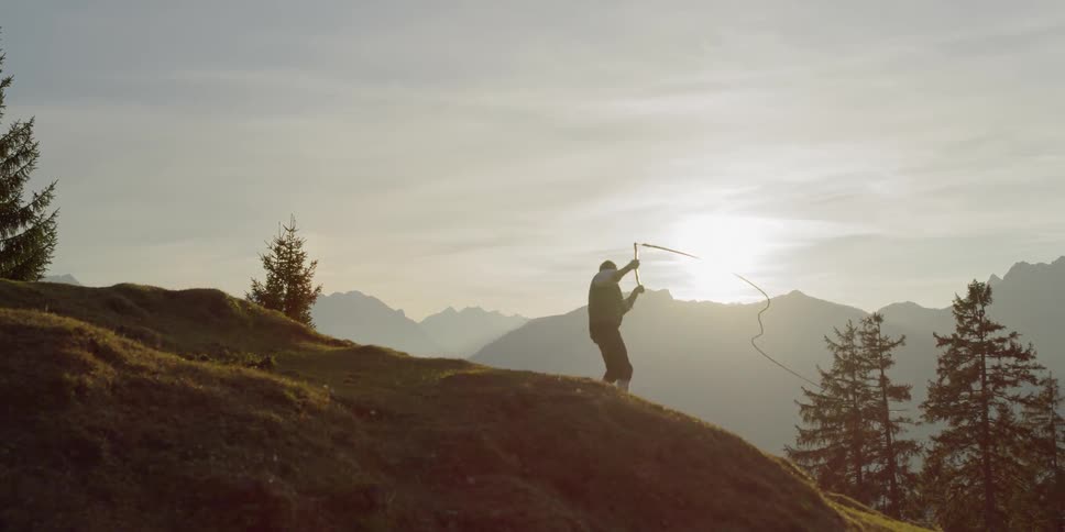 A man swings a whip while standing on a hillside