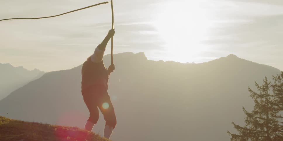 Male standing in a field in the mountains whipping a whip around