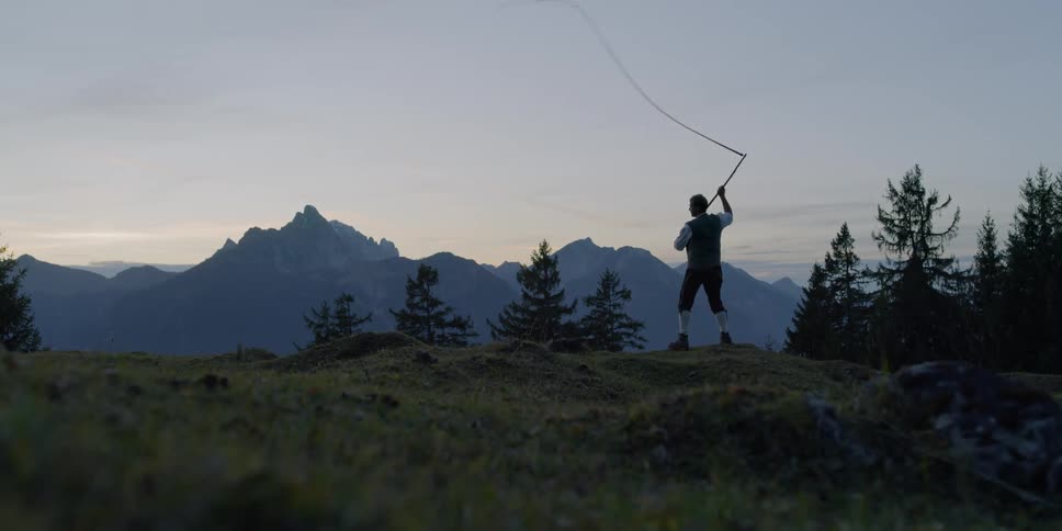 A man swings a whip with mountains in the distance