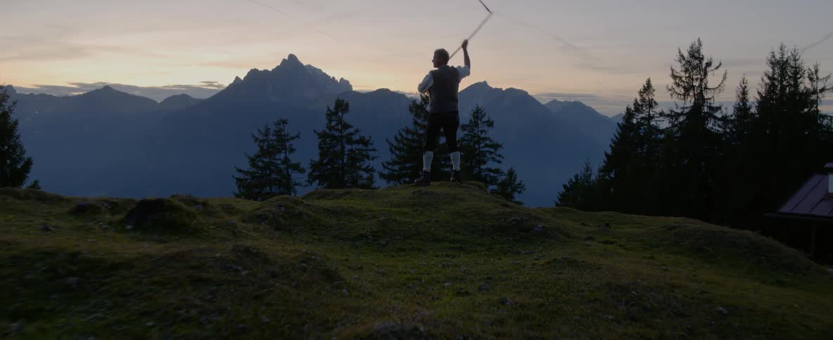 A man stands on a hill and swings a whip