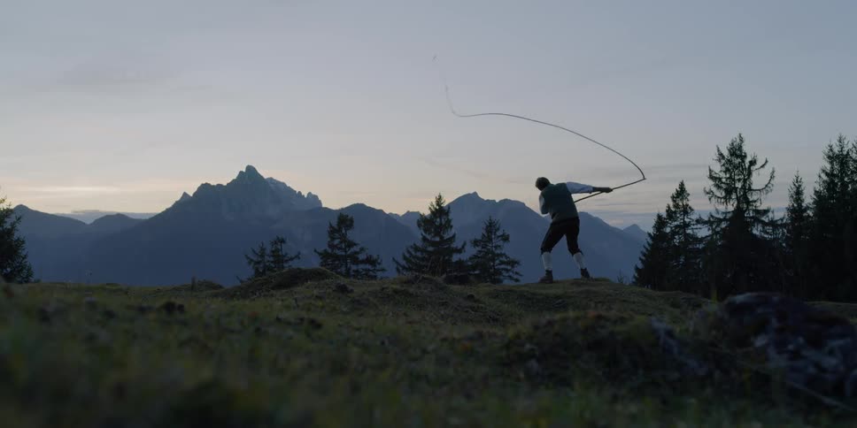 A man stands on a hill using a whip