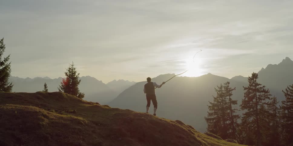 Man swings whip on a hill at sunset
