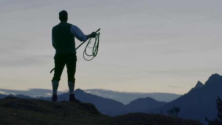 A man with a whip stands on a hill
