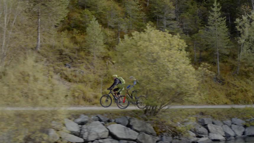 Two cyclists cycle on the road next to the lake in the daytime