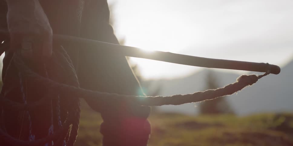 A person holds a whip with a mountain in the background