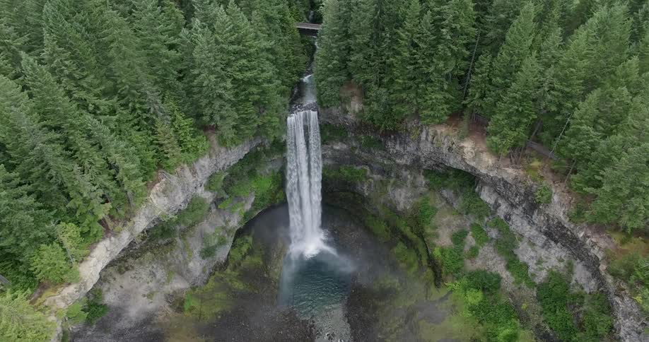 A waterfall flowing from a tree-lined rim and crashing down in to a pool
