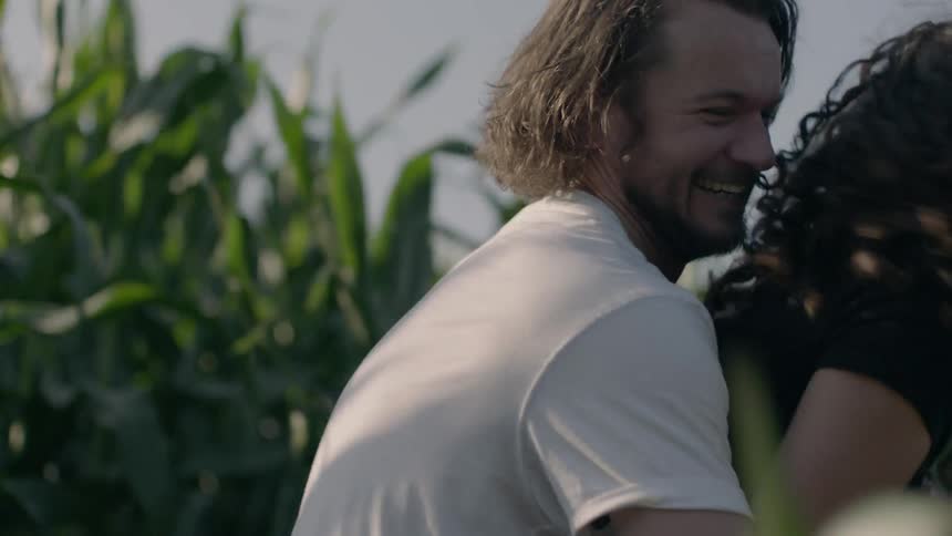 A man chases a woman through a field of corn and embraces her