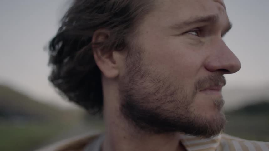 Close up of a male in a field looking around and hair blowing in the wind