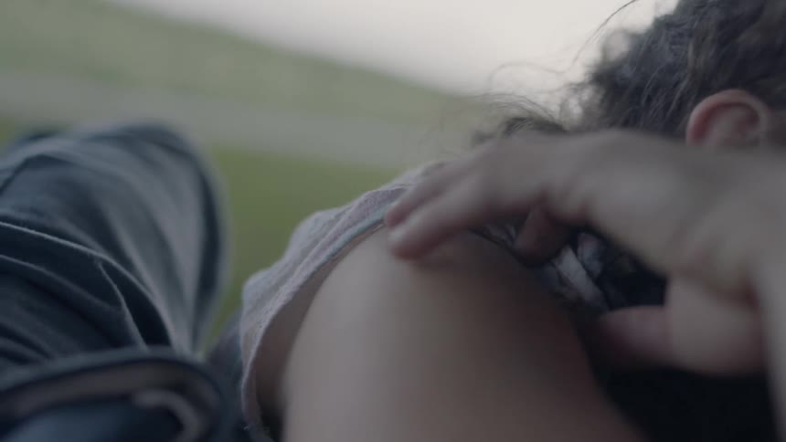 A young woman with her arms folded in front of her caresses her own arm as she stares off in the distance