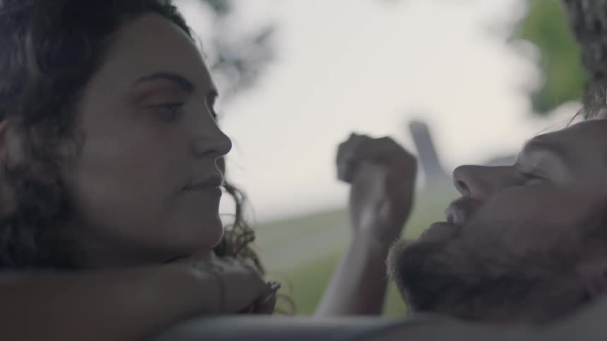 A woman rests on a mans chest as he lay against a tree