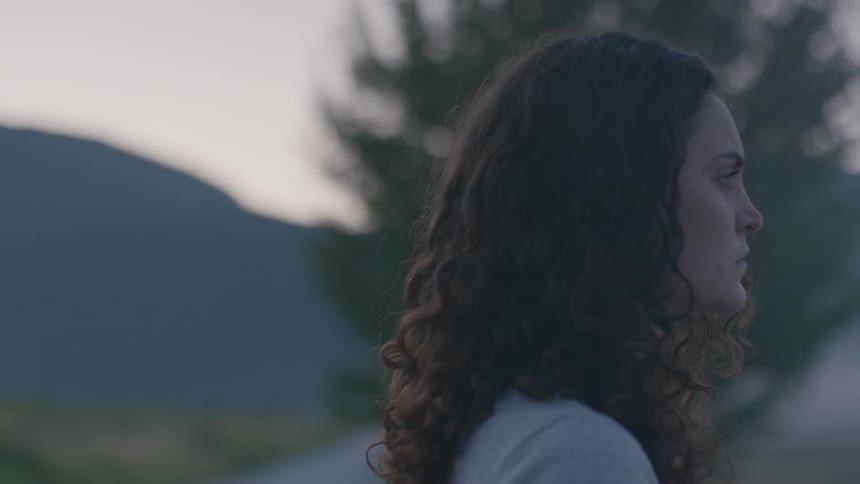 A female caucasian walking outside near a tree and mountains