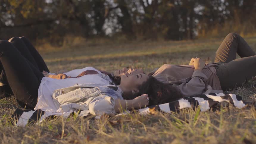 Three women lay on a striped blanket in a grassy field