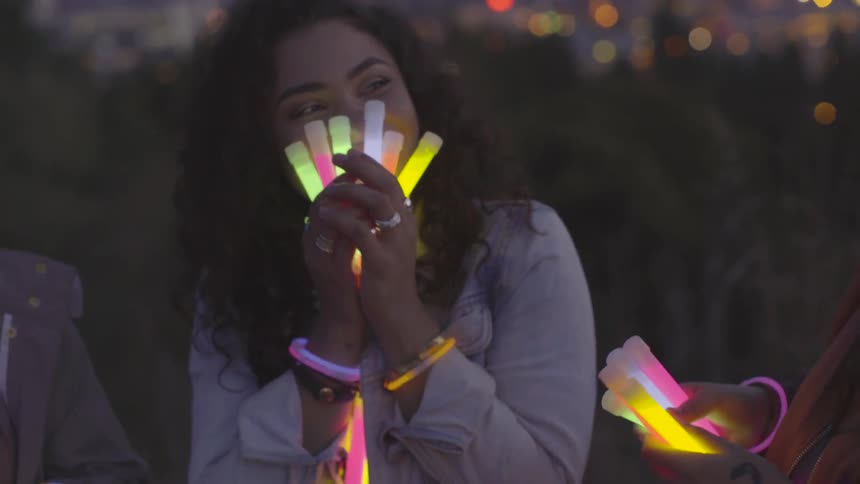 Two hispanic girls holding glow sticks and giggling together