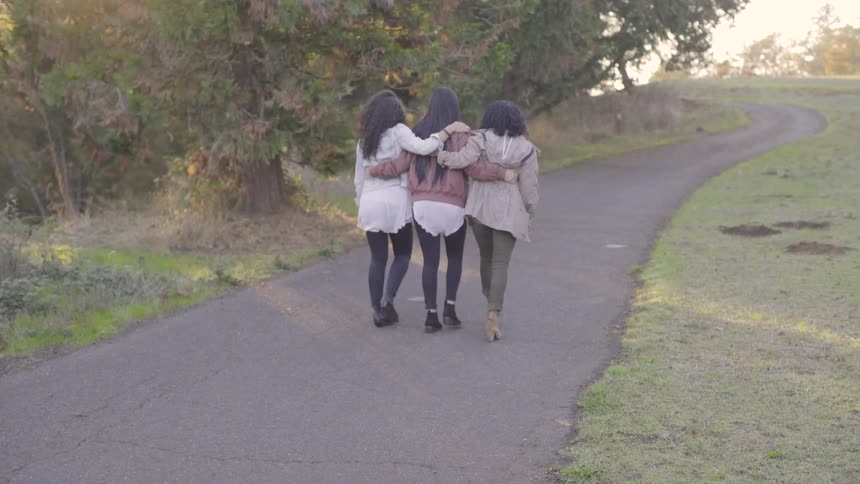 Three friends walk down a path holding each other
