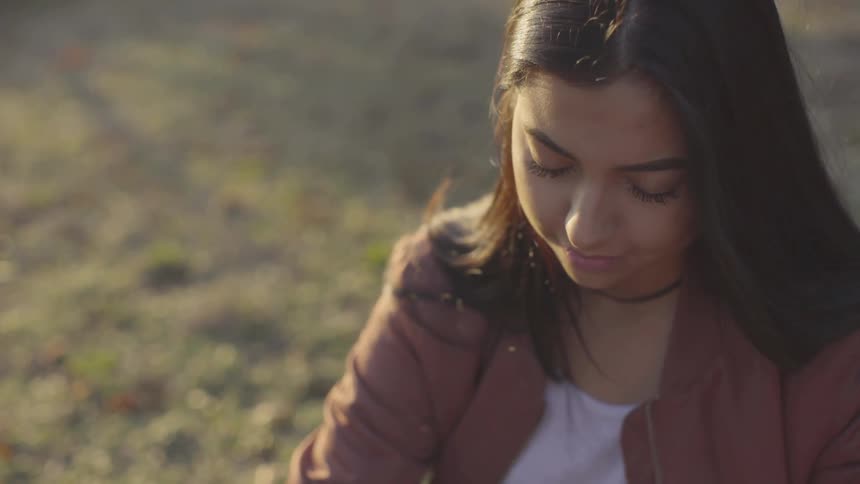 A woman sitting on the grass looking down with the sun in her face