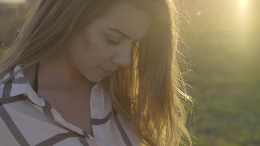 A woman is looking down outside while the sun sets