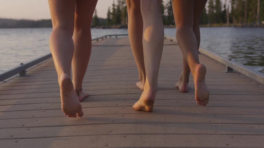 A group of barefoot young women walking along a pier