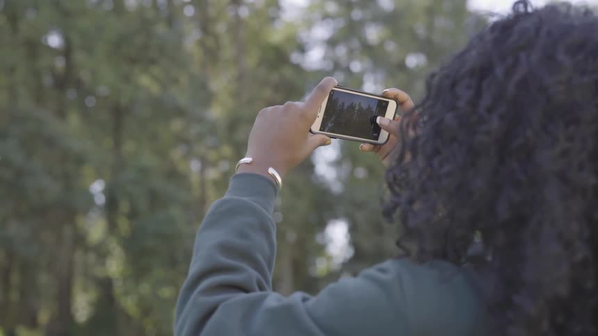 A woman holds up her phone and turns it to get the best angle to photograph the trees
