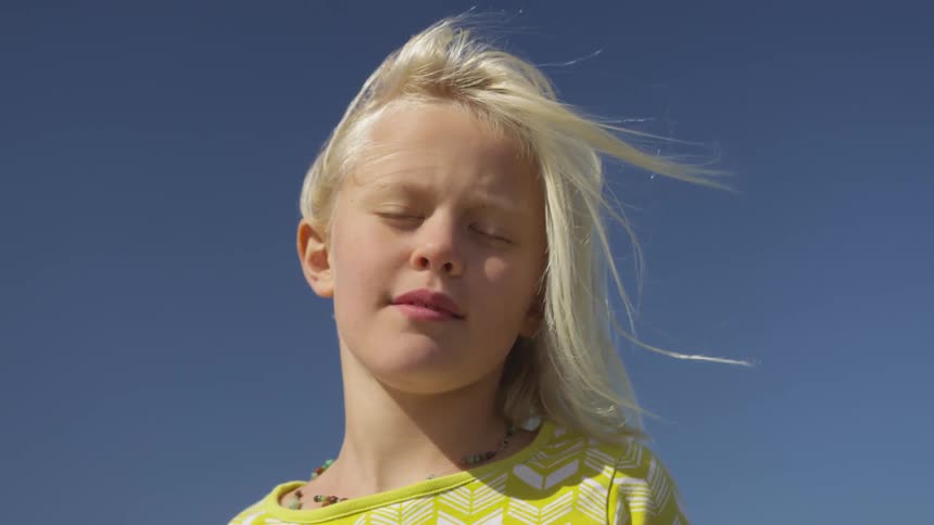 A young blonde girl standing outdoors in the window with her eyes closed