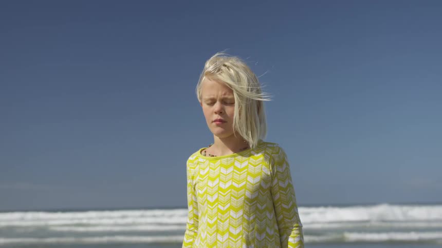 A girl standing on the beach with her eyes close and the ocean in the background