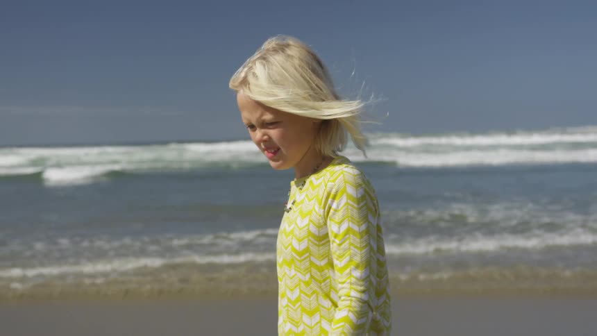 The wind blows through a blonde girls hair as she walks on a sandy beach