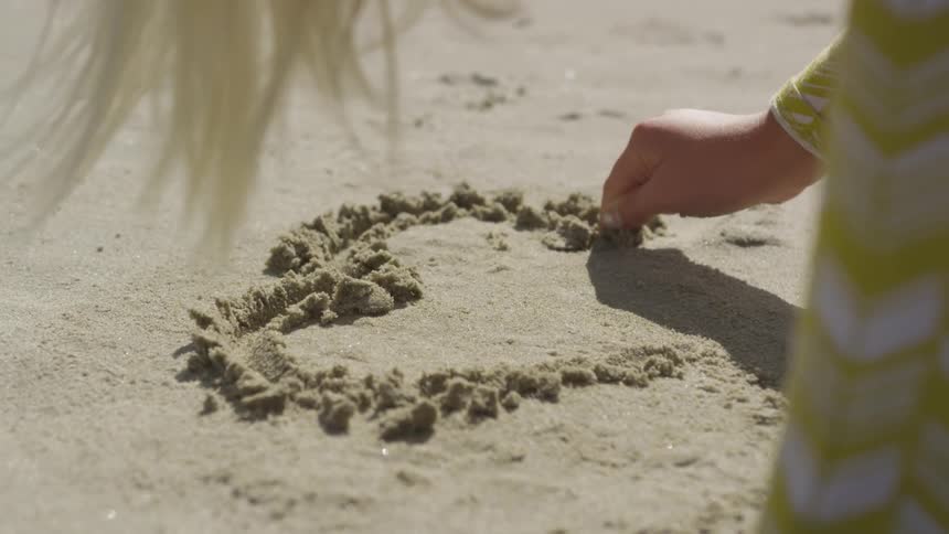 Girl draws heart on beach with her fingers