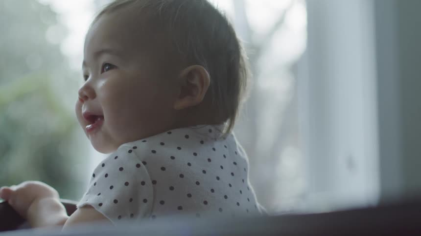 A baby is smiling while looking out a window