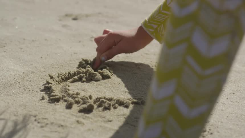 Girl draws heart in the sand