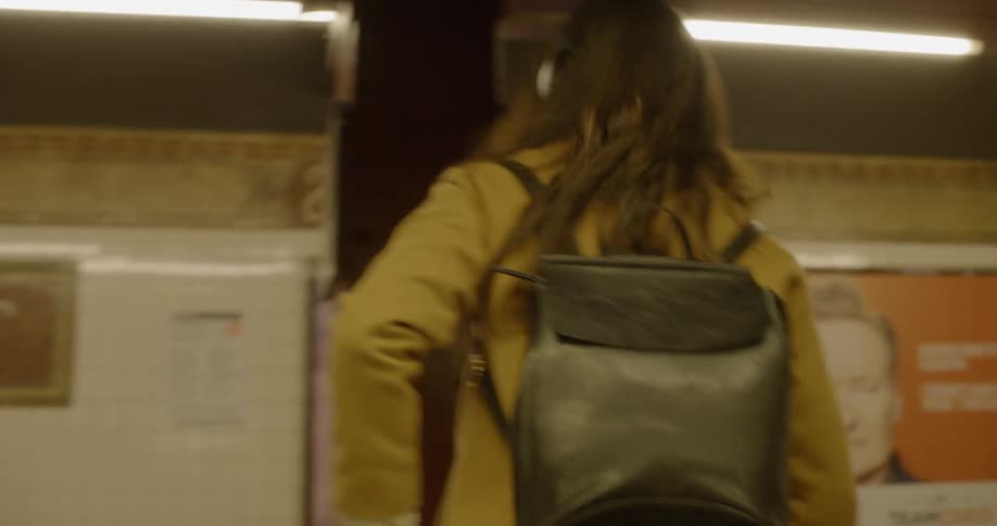 A woman walking out of a train with headphones and a book bag