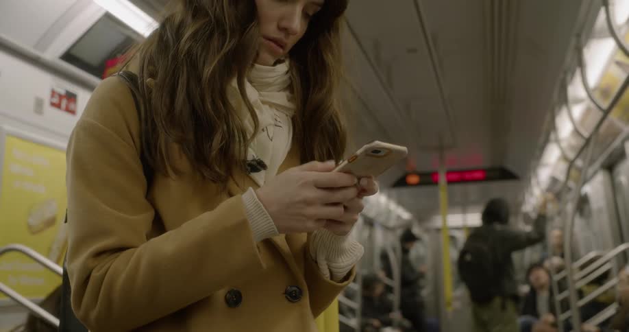 A white woman checks her smartphone on a subway car