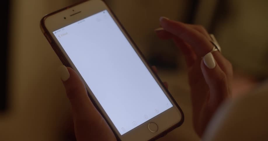 A woman with two rings on her fingers on her right hand scrolls upwards on a blank white screen on the smart phone held in the left hand
