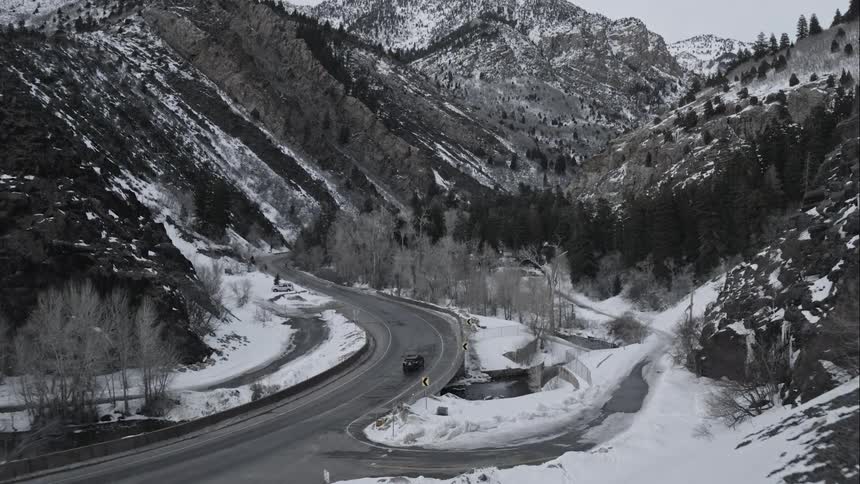 A car drives down a road in snowy mountains