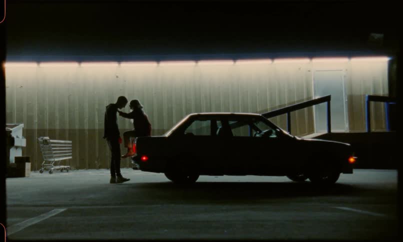 A man and a woman flirt on the back of a car
