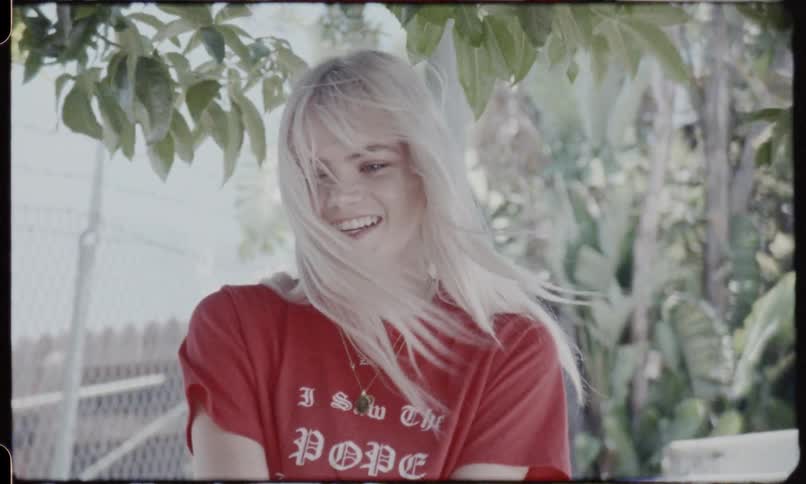 A blonde woman wearing an i saw the pope top talks any smiles on a sunny day