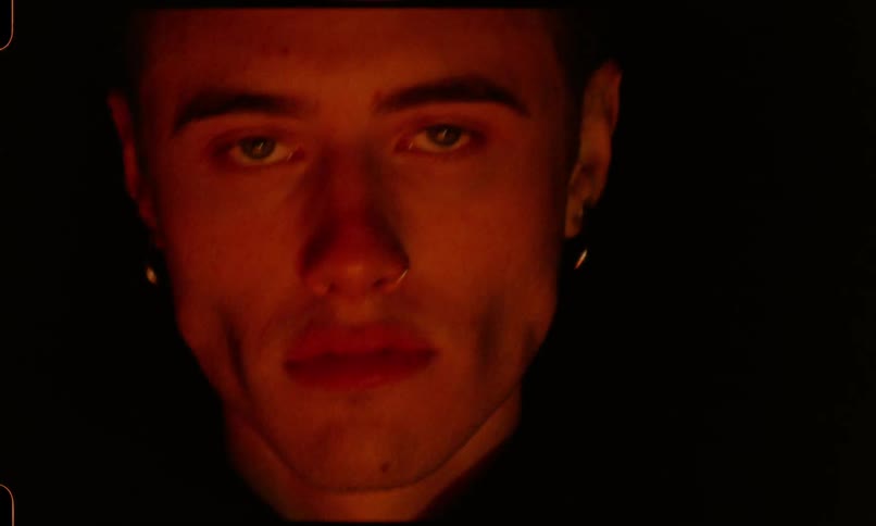 Man stares at the camera in front of flickering red lights