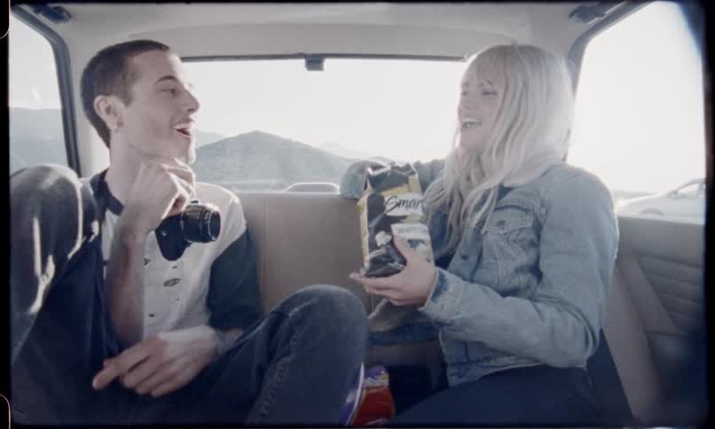 A man and a woman eat in the back seat of a car