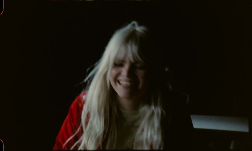 A woman laughing and playfully kicking a man while sitting on a car at night