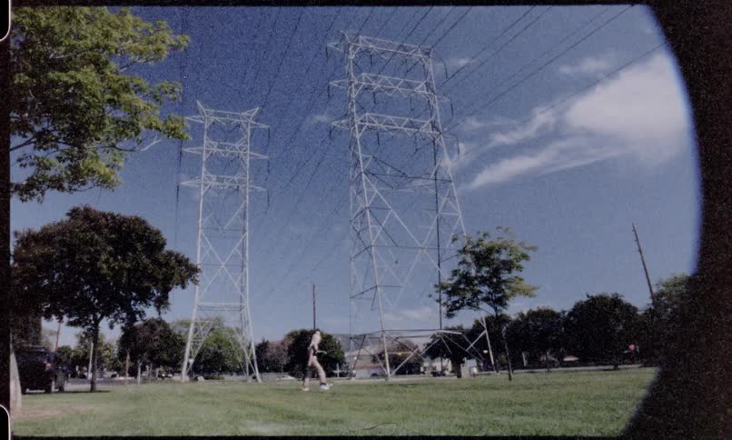 A man and woman hold hands as they walk on the grass under power lines