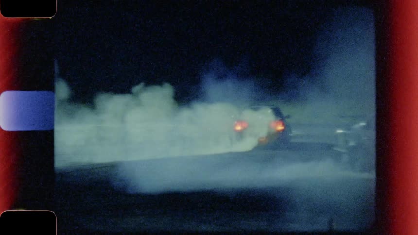 A car drifts around a corner spraying smoke