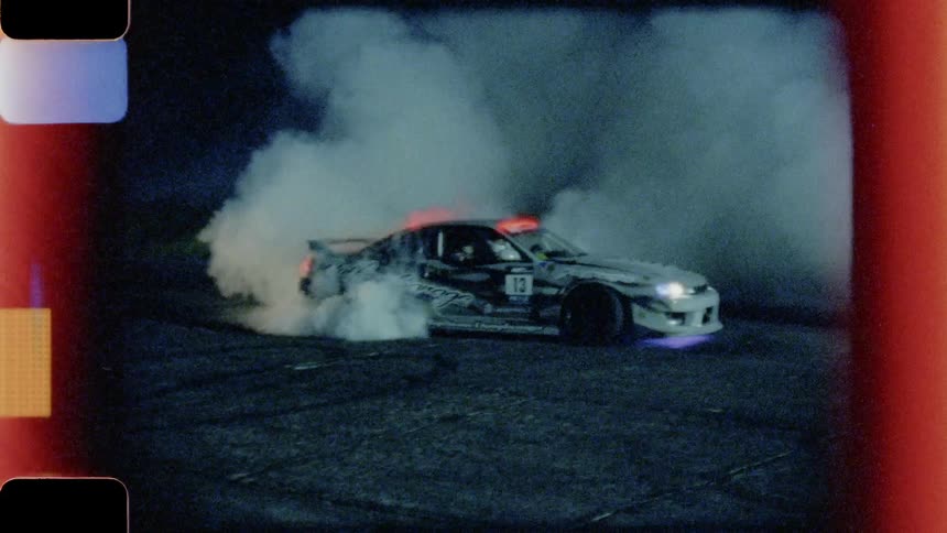Racing cars burn rubber off their tires in preparation for the event at night
