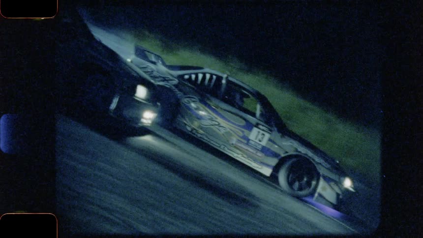 Drivers oversteer while maintaining control and driving therace cars through the entirety of a corner at night