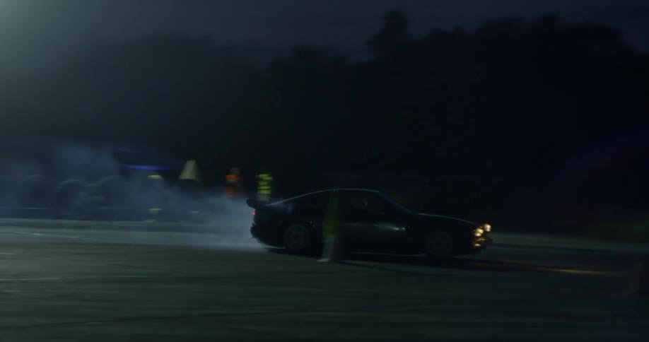 A car with smoking tires traveling down a dragstrip at night