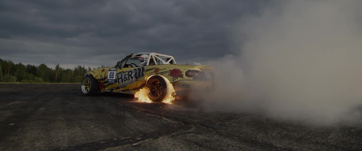 A stunt car has flames spinning around the back tire